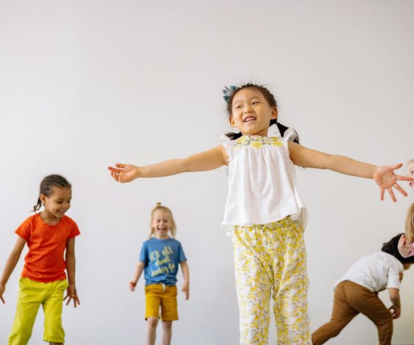 Group of happy children doing a simple yoga pose on colorful mats in a bright room.